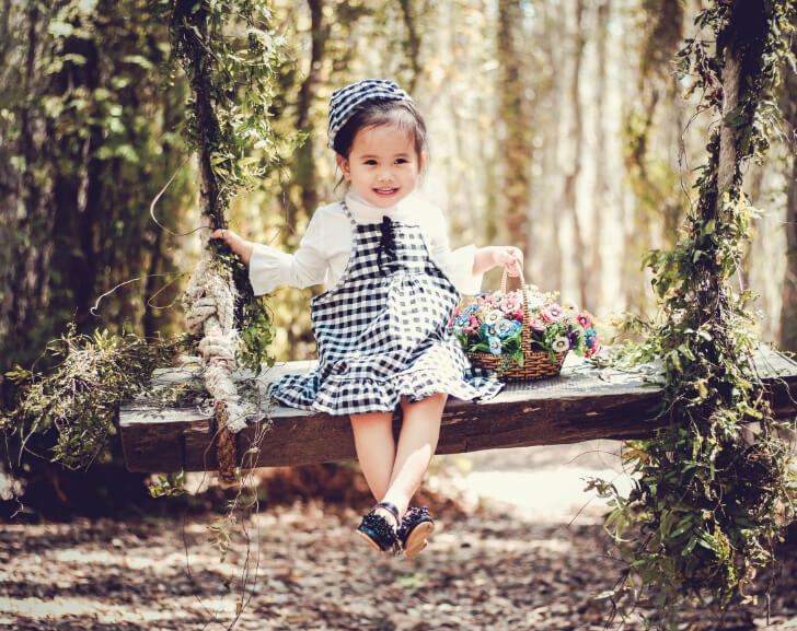 little girl smiling holding basket of flower sitting on wooden bench baby girl names